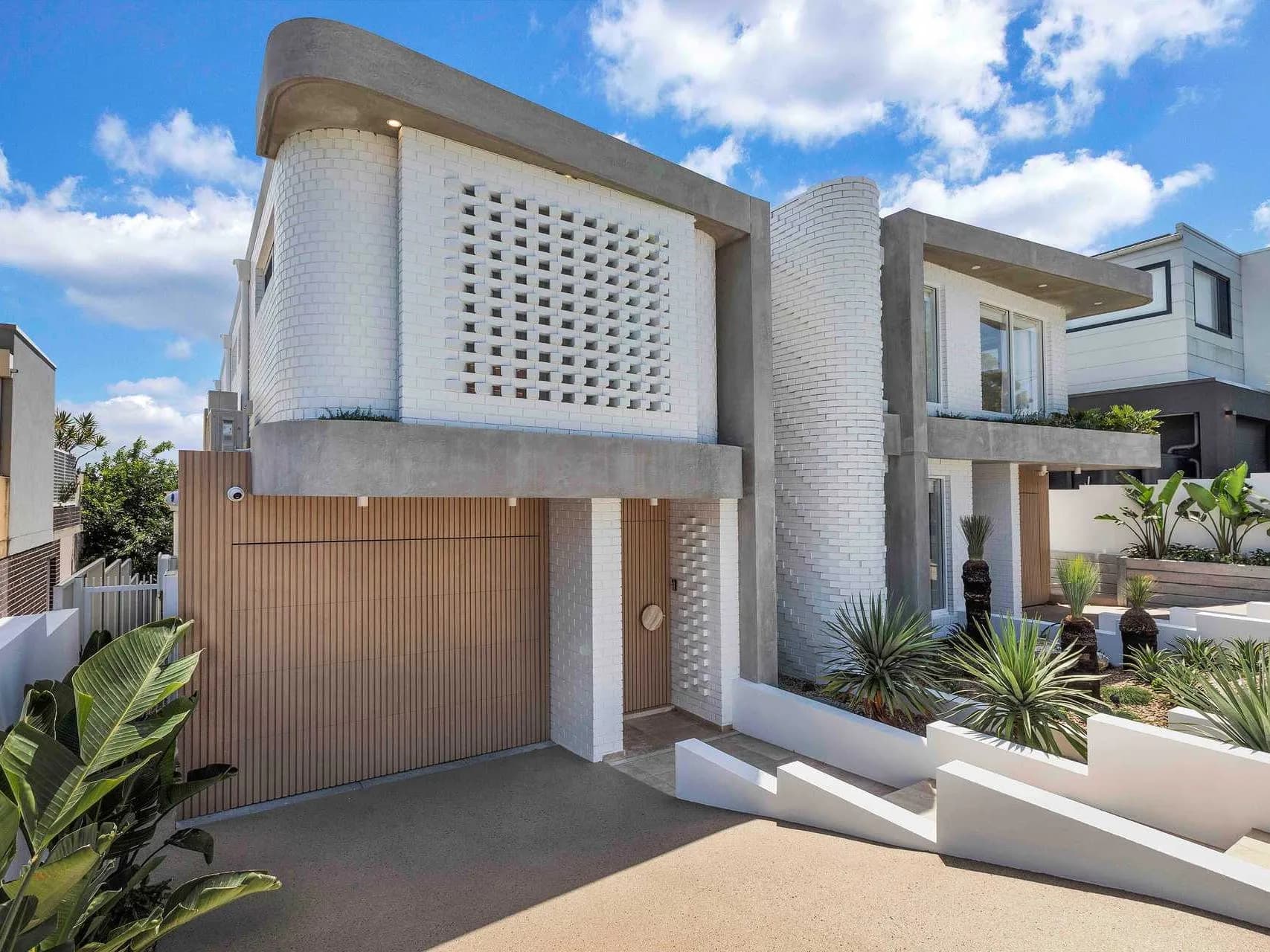 Street elevation of Hillary, a completed white-brick duplex in Matraville with a curved breeze-block screen and battened timber garage door